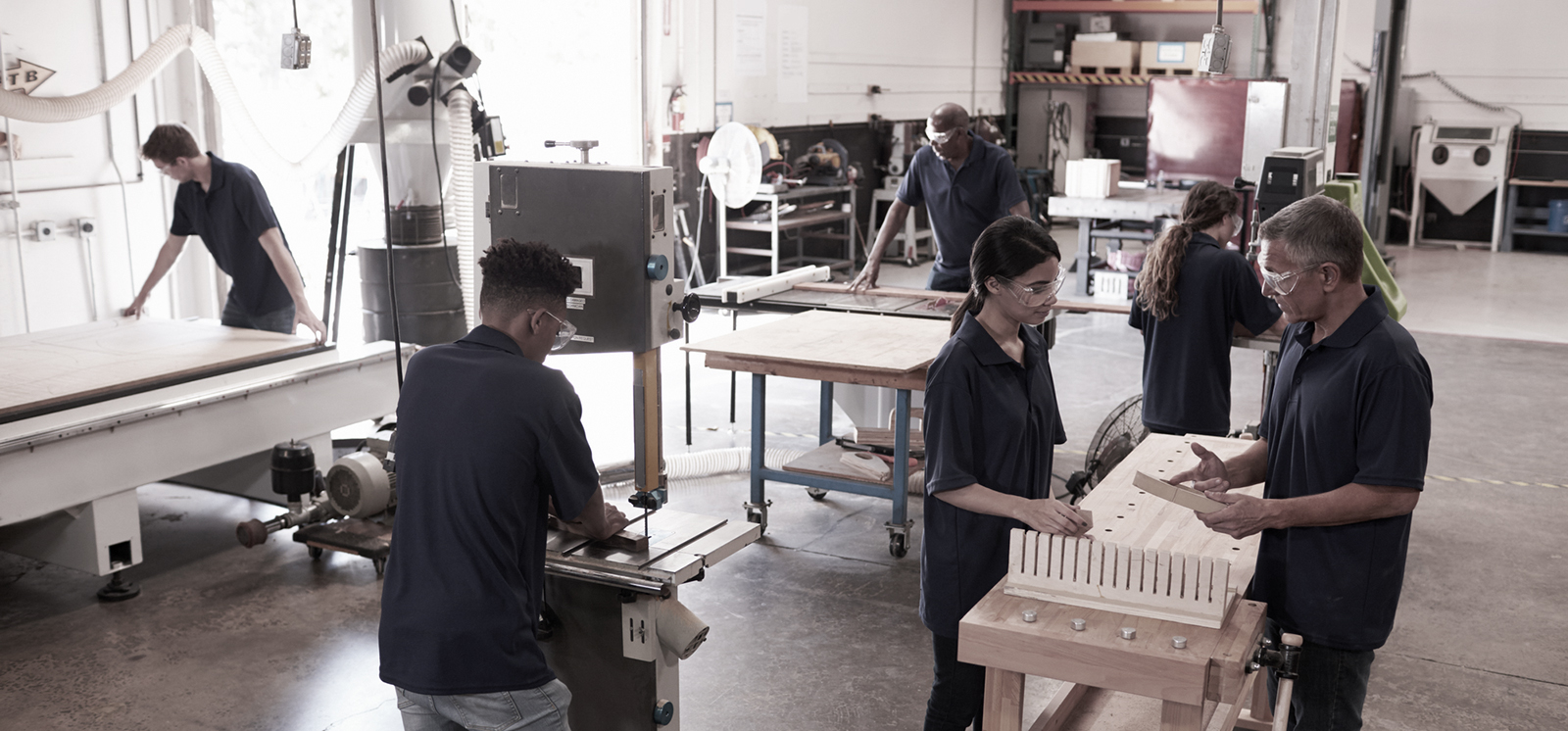 Carpenters Working On Machines In Busy Woodworking Workshop